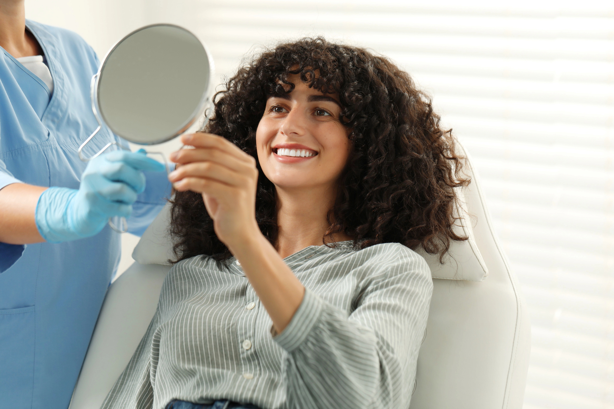 Woman smiling and admiring her new dental veneers in a mirror